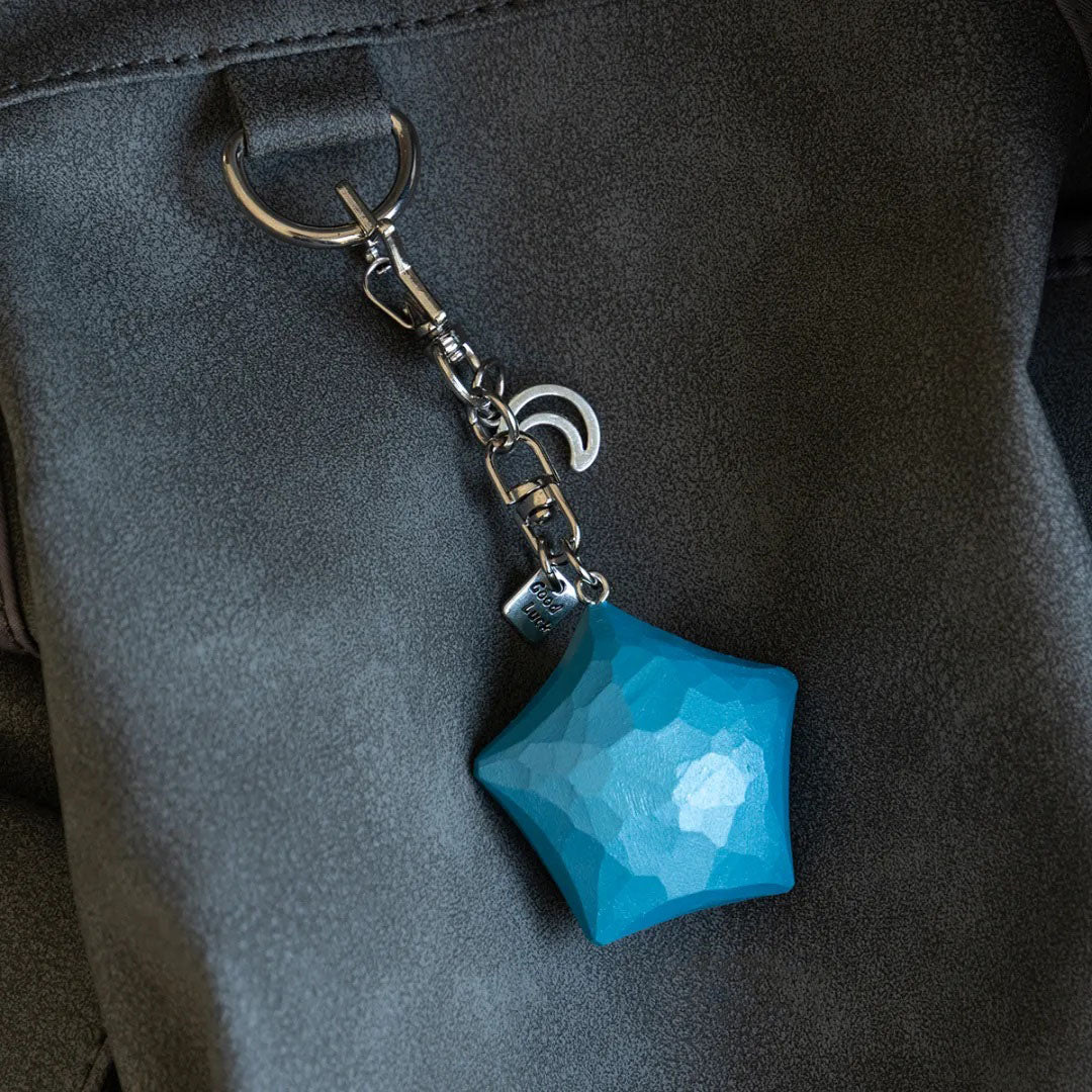 Blue wooden star keychain hanging from a dark bag
