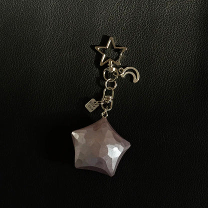 Dusty rose wooden star keychain with metal moon charm and Good Luck tag on a black background