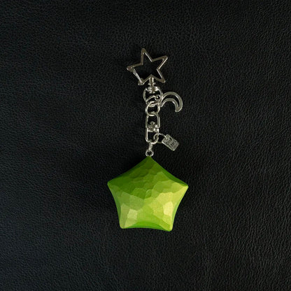 Green hand-carved wooden star keychain with metal charms on a black background