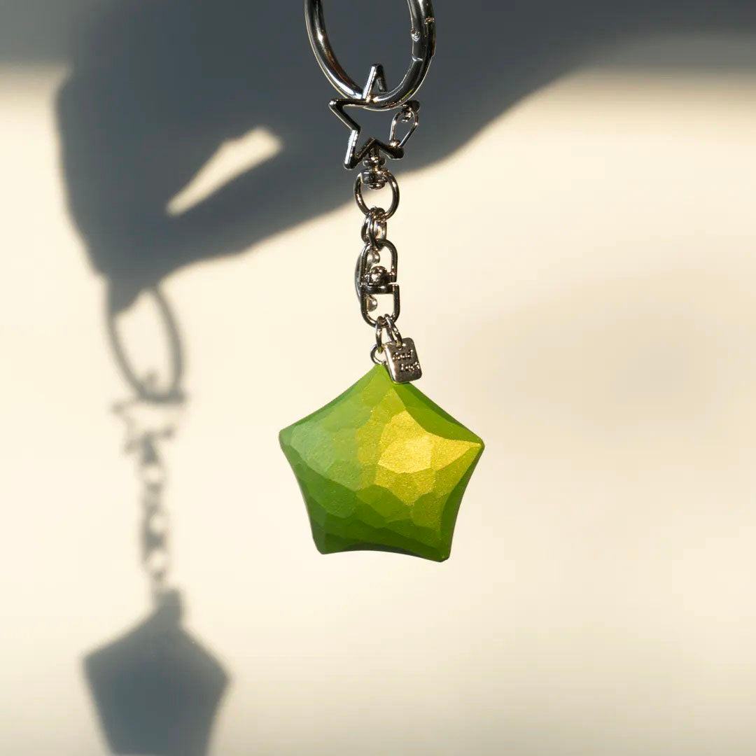 Green wooden star keychain hanging in sunlight with its shadow visible