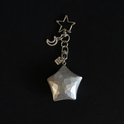 Silver hand-carved wooden star keychain with crescent moon charm on a black background