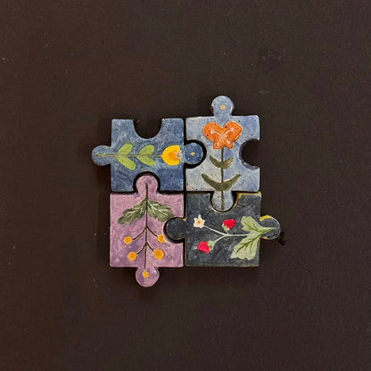 Four hand-painted clay puzzle magnets joined together with colorful floral and botanical designs