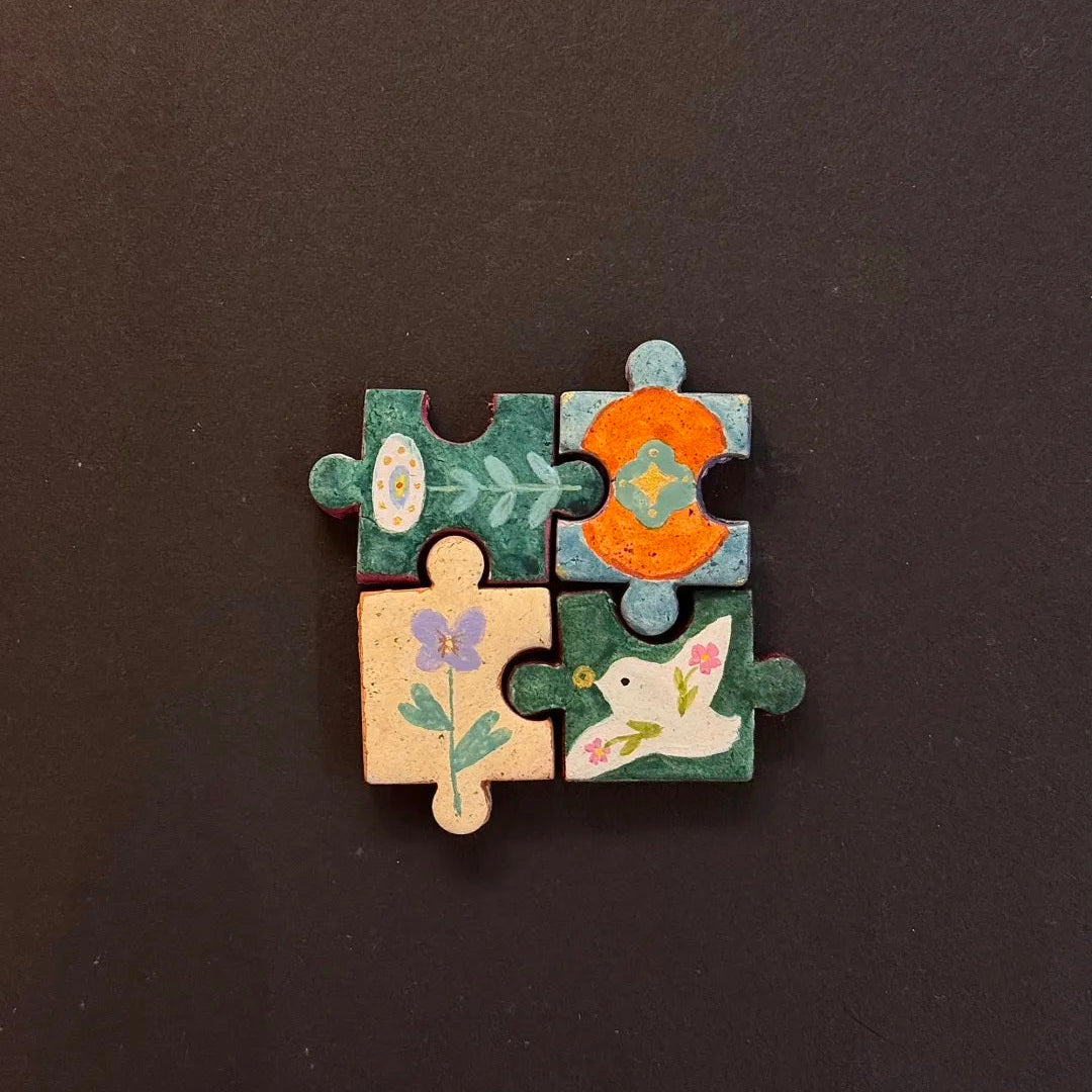 Four hand-painted clay puzzle magnets connected together featuring colorful flowers in warm tones