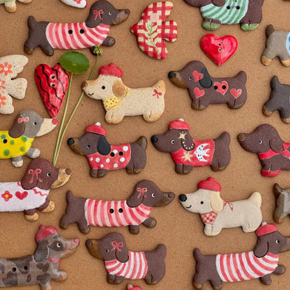 Close-up of handmade ceramic dachshund magnets wearing colorful sweaters, hats, and scarves