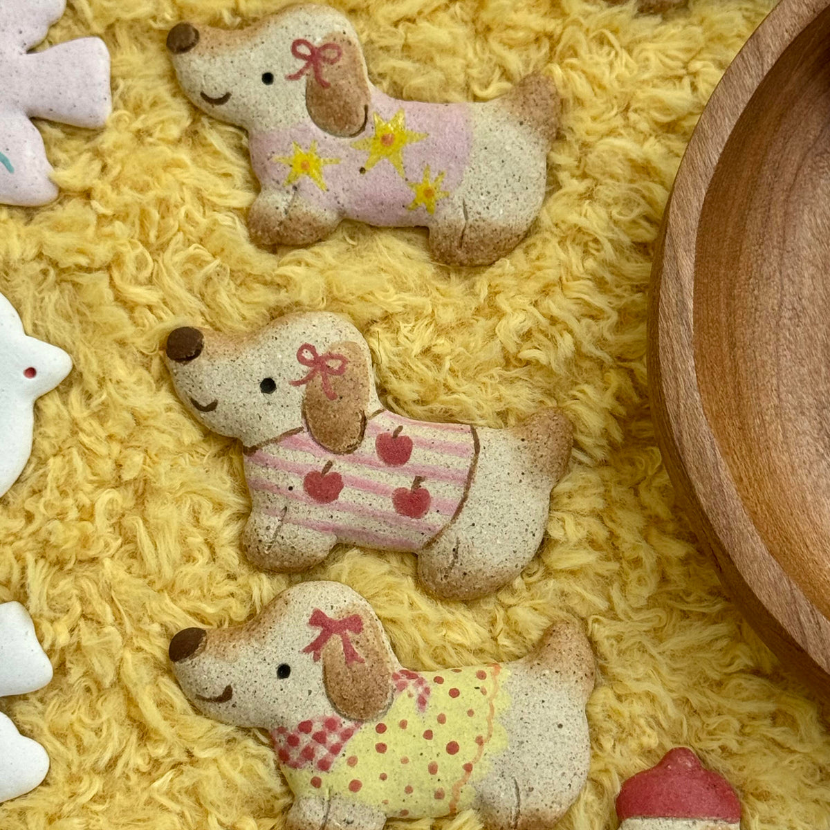 Close-up of handmade ceramic dachshund magnets with colorful sweaters and scarves on a yellow textured background
