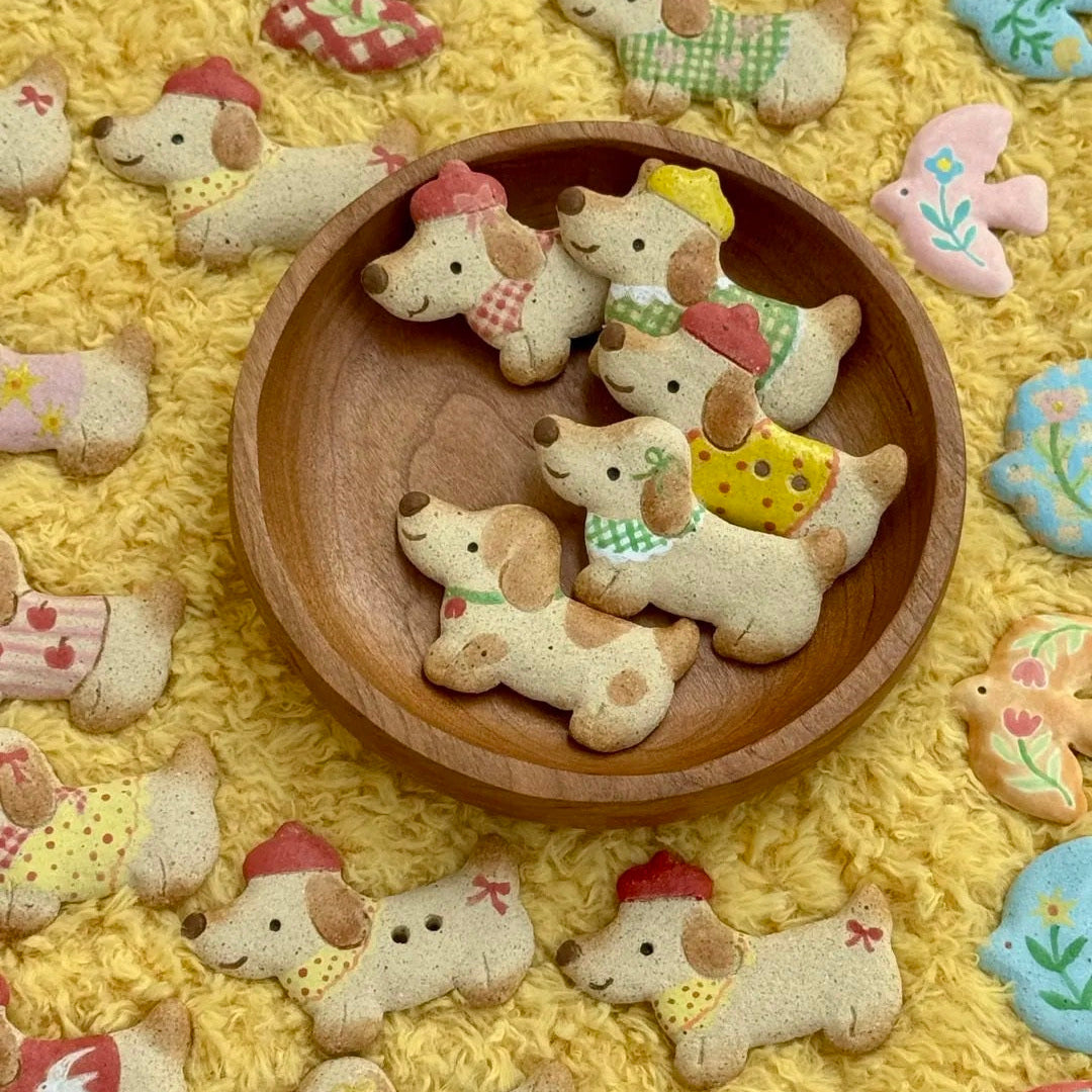 Handmade light-colored ceramic dachshund magnets displayed together on a round wooden tray