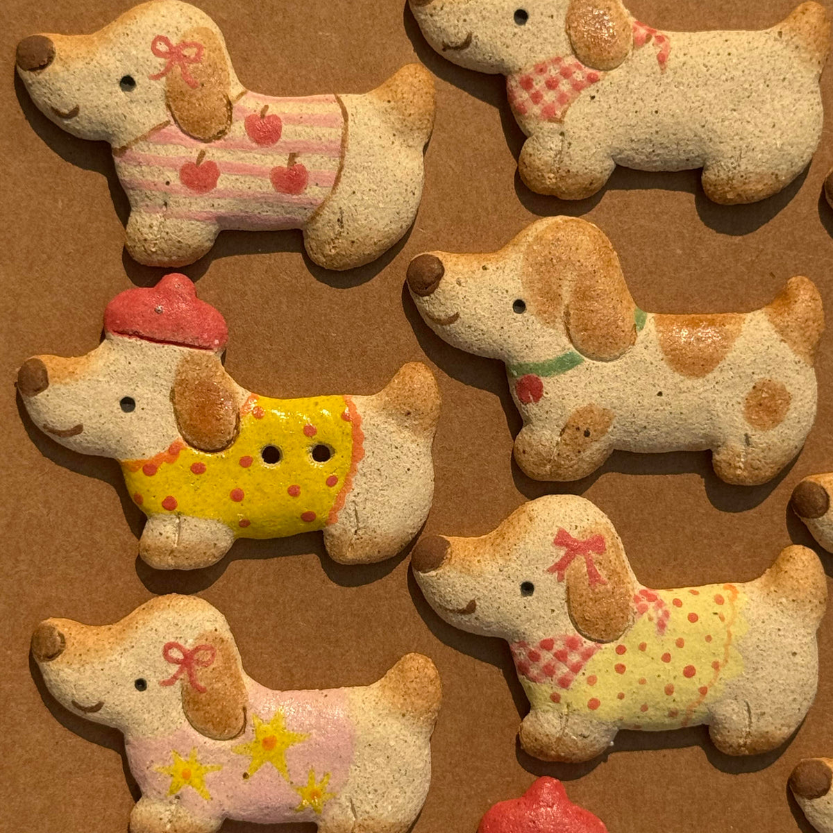 Assorted light-colored ceramic dachshund fridge magnets wearing colorful outfits displayed on a wooden surface
