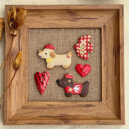 Handmade ceramic dachshund magnets displayed inside a wooden frame with colorful decorative pieces