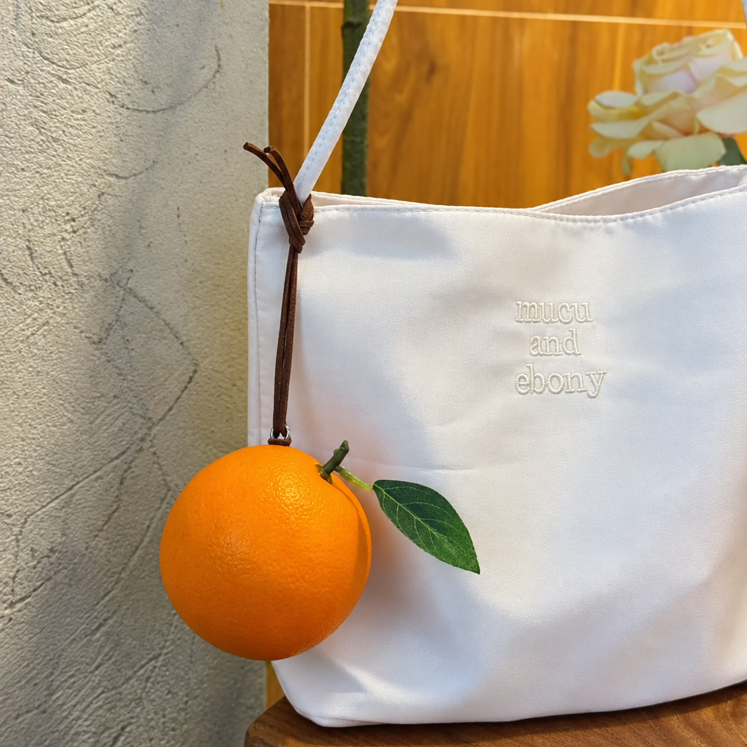 Lifelike handmade foam orange charm with a green leaf hanging from a white tote bag.