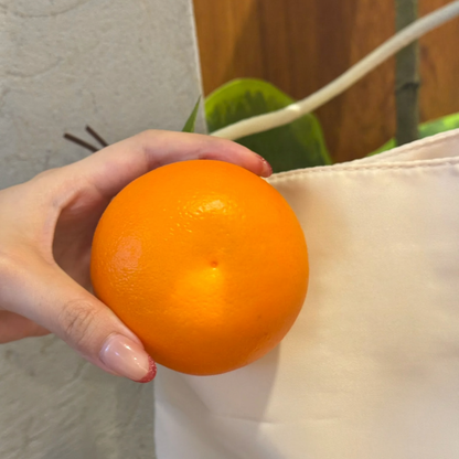 Lifelike handmade foam orange charm held in a hand, showing its realistic peel texture.