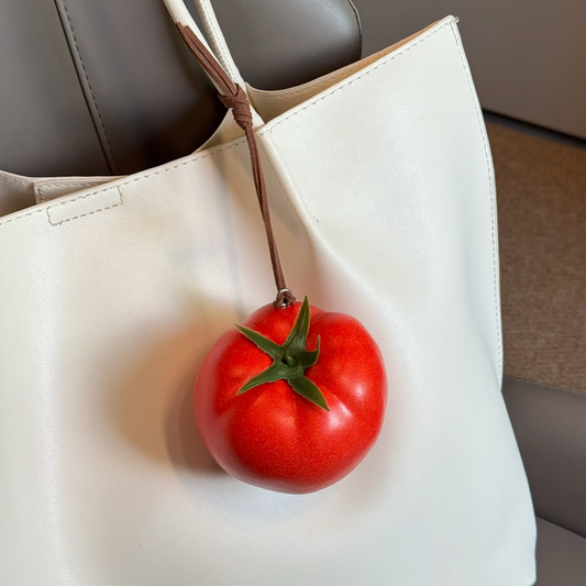 Lifelike handmade foam tomato charm with a green stem hanging from a white tote bag.