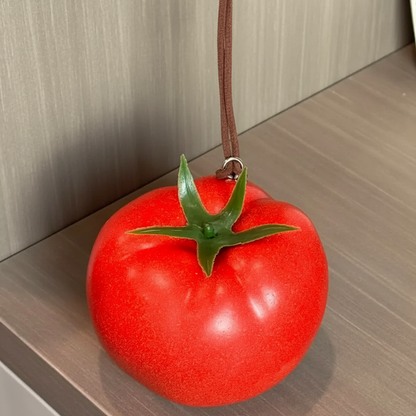 Close-up of a lifelike foam tomato charm showing its red surface and green stem.