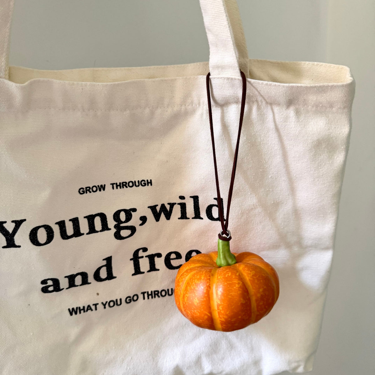Mini foam pumpkin hanging charm attached to a canvas tote bag.