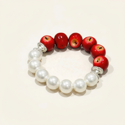 Handcrafted beaded bracelet featuring half glossy red apples and half lustrous white pearls on a minimalist cream background.