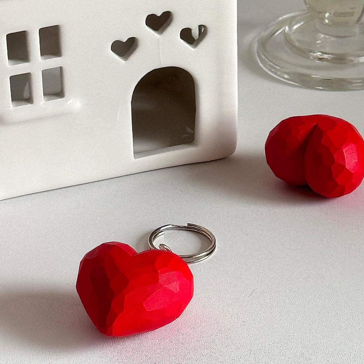Red wooden heart keychain with metal keyring displayed on a desk beside miniature decor