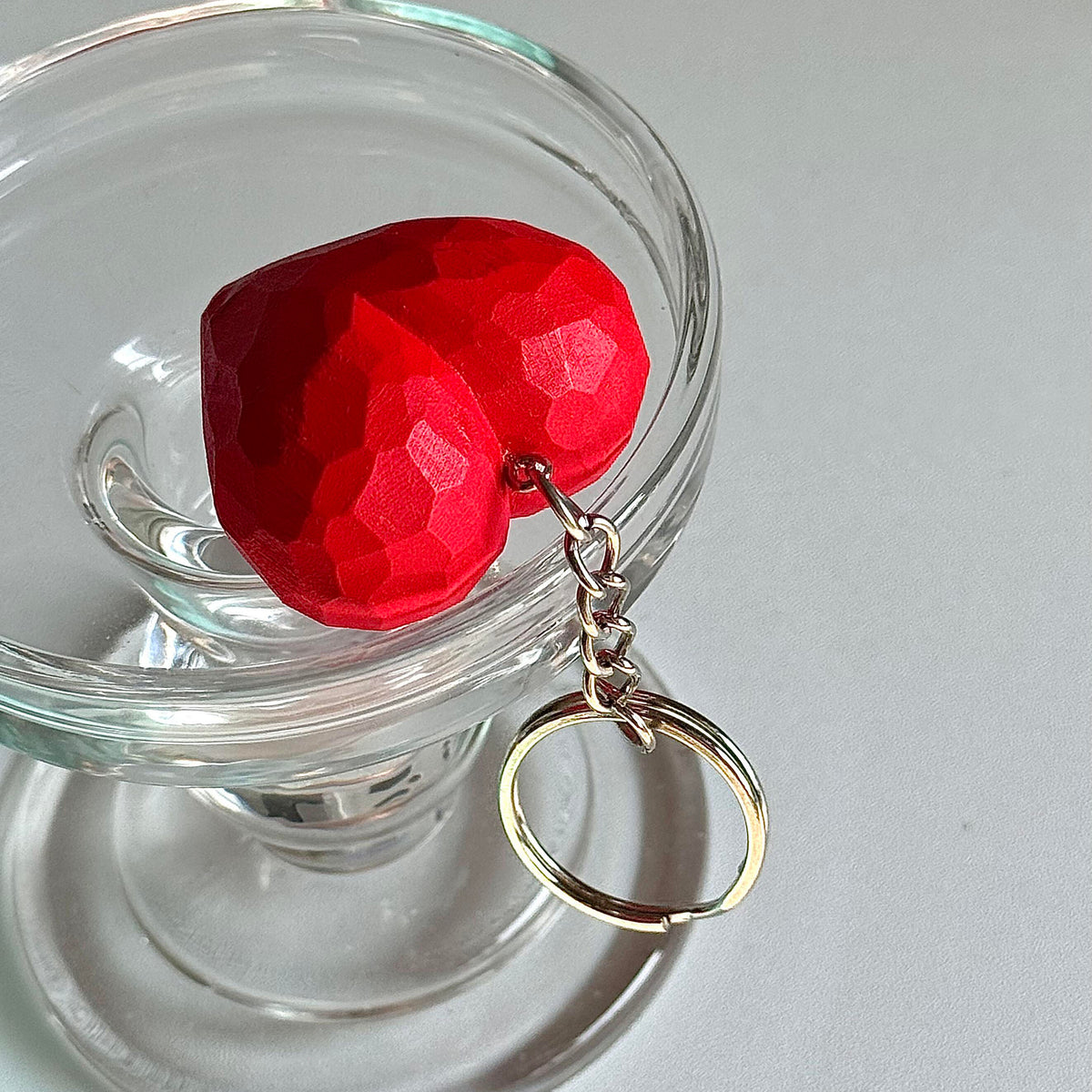 Red faceted wooden heart keychain displayed inside a clear glass container