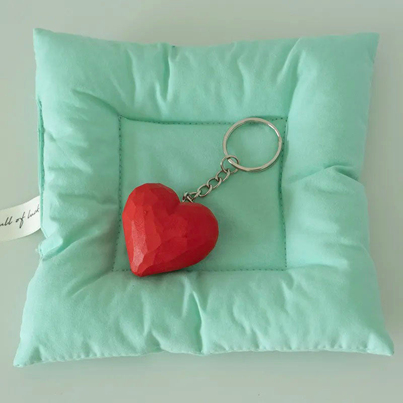 Red wooden heart keychain with metal ring displayed on mint green fabric