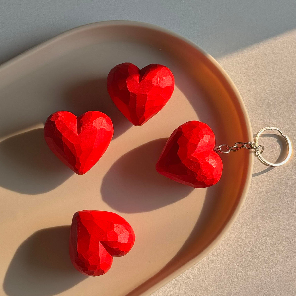 Red faceted wooden hearts displayed on a tray in warm sunlight, with one attached to a metal keyring