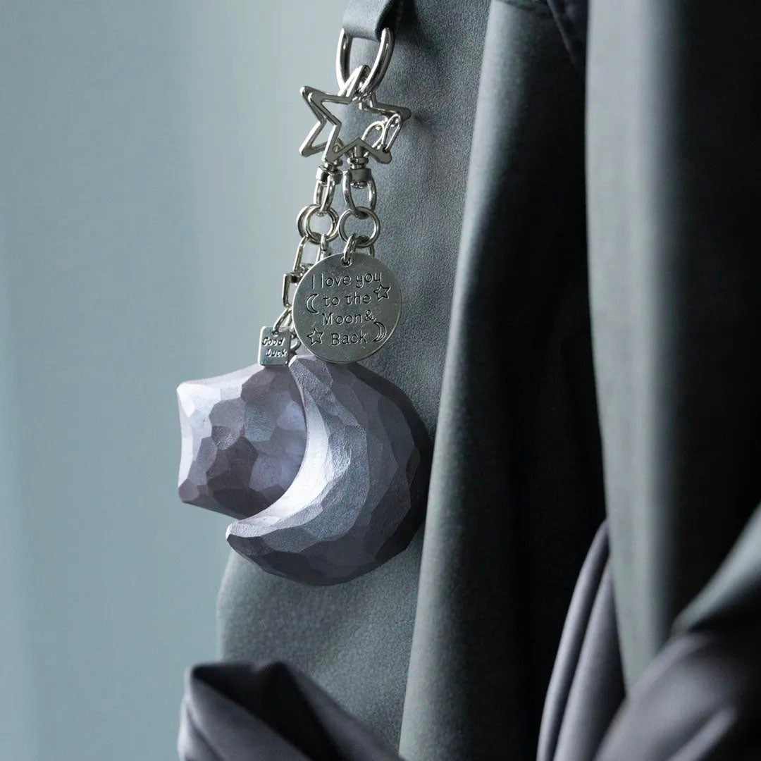 Dusty Rose wooden star and crescent moon keychains hanging together from a dark bag