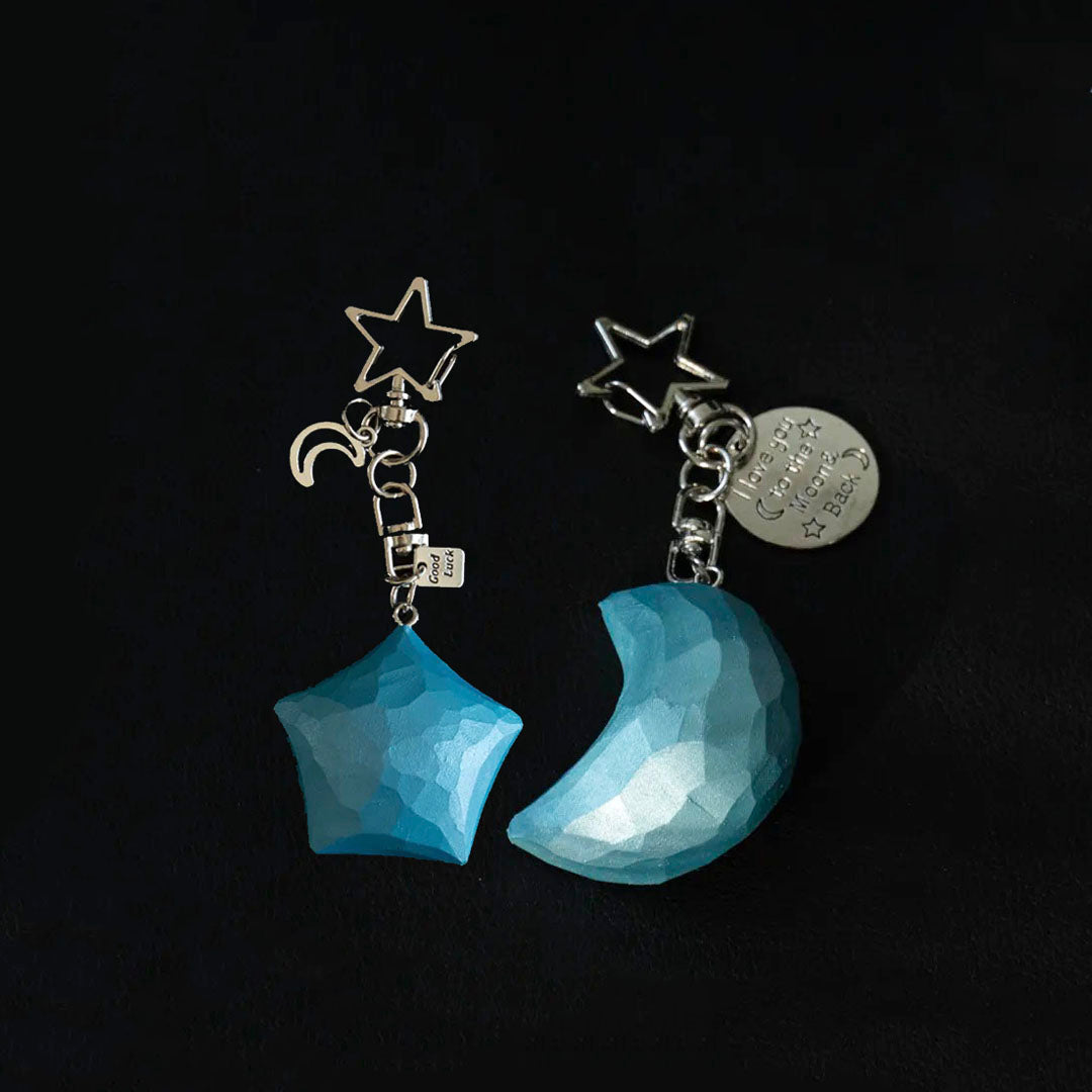 Matching blue wooden star and crescent moon keychains with metal charms on a dark background