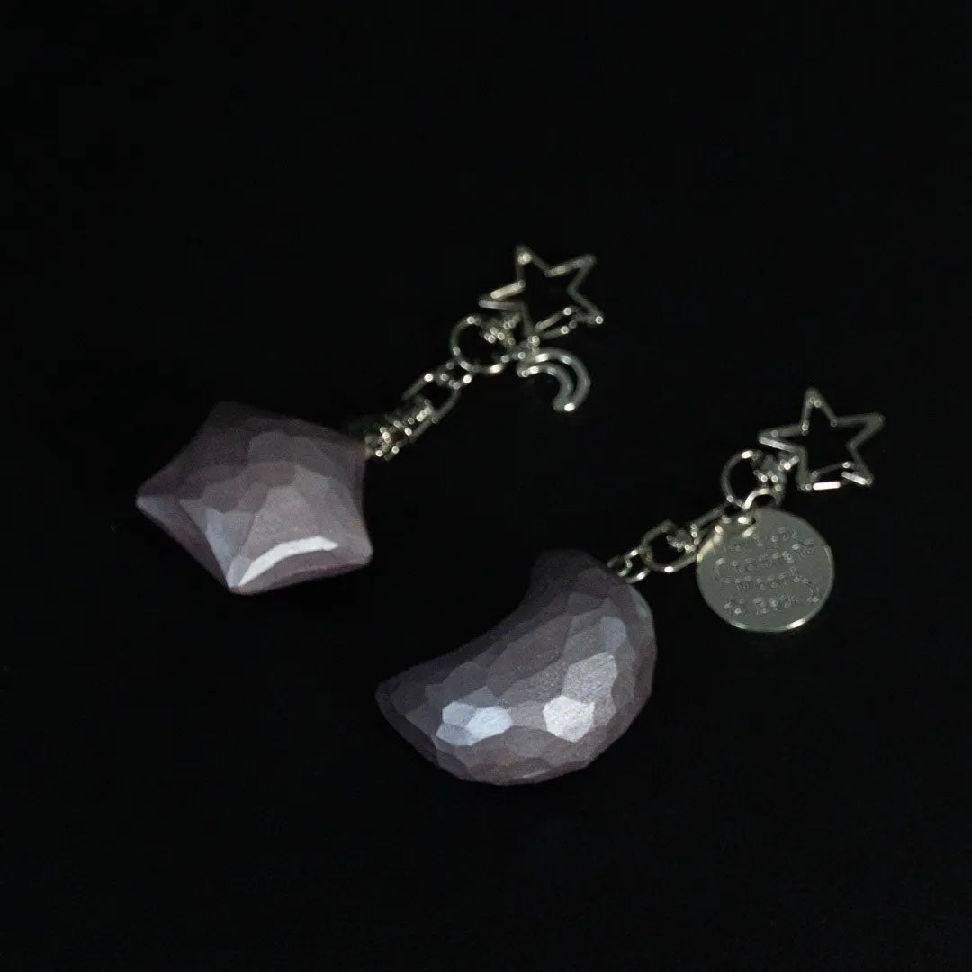 Dusty rose wooden star and crescent moon keychains displayed together on a black background