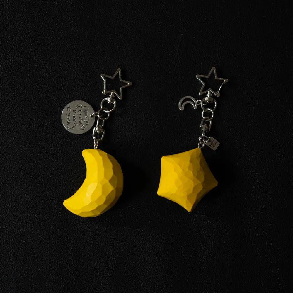 Matching yellow wooden star and crescent moon keychains with metal charms on a dark background